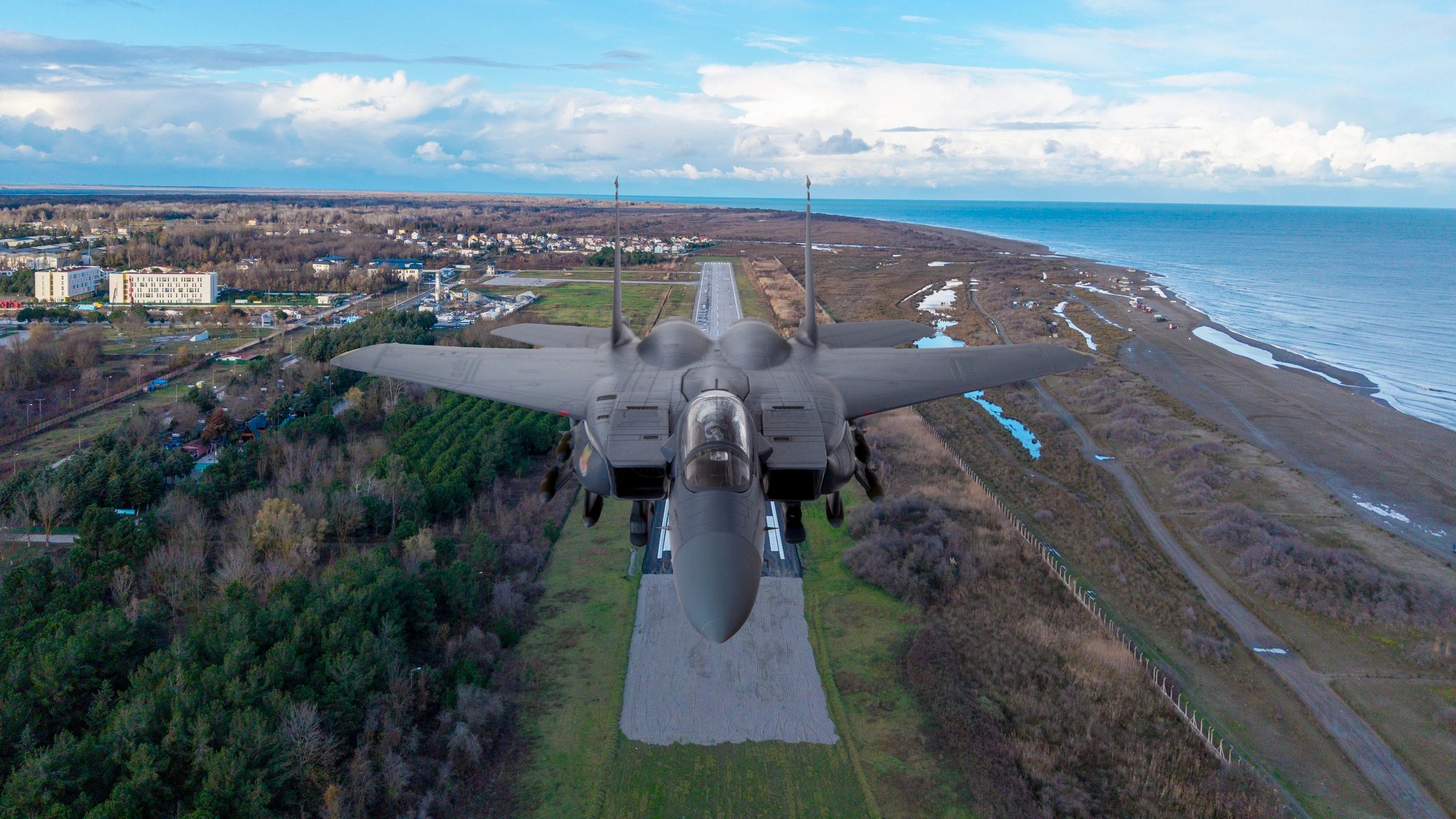 F-15 eagle fighter jet flying over runway and coastline